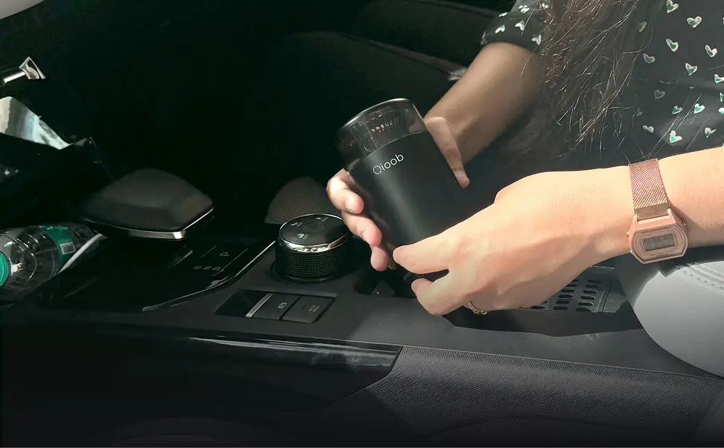 A person placing the car perfume diffuser in the car's cup holder
